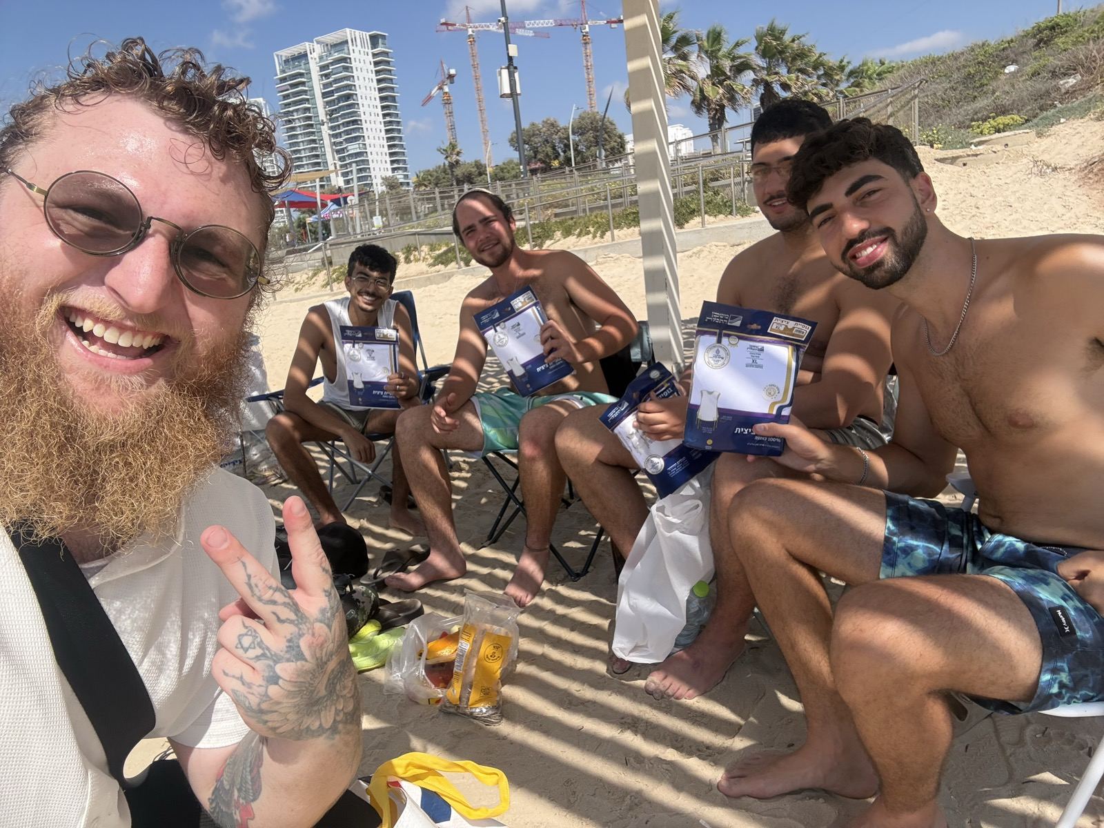 A group of friends in beach chairs smiling and holding blue tefillin bags