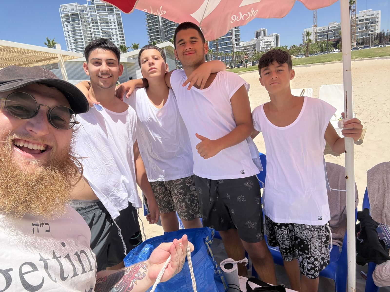 A group of teenage boys posing with a smiling man under a beach umbrella