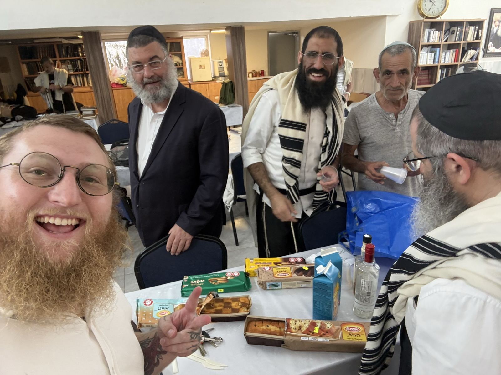 Men in tallitot gathered around a table with food and drinks