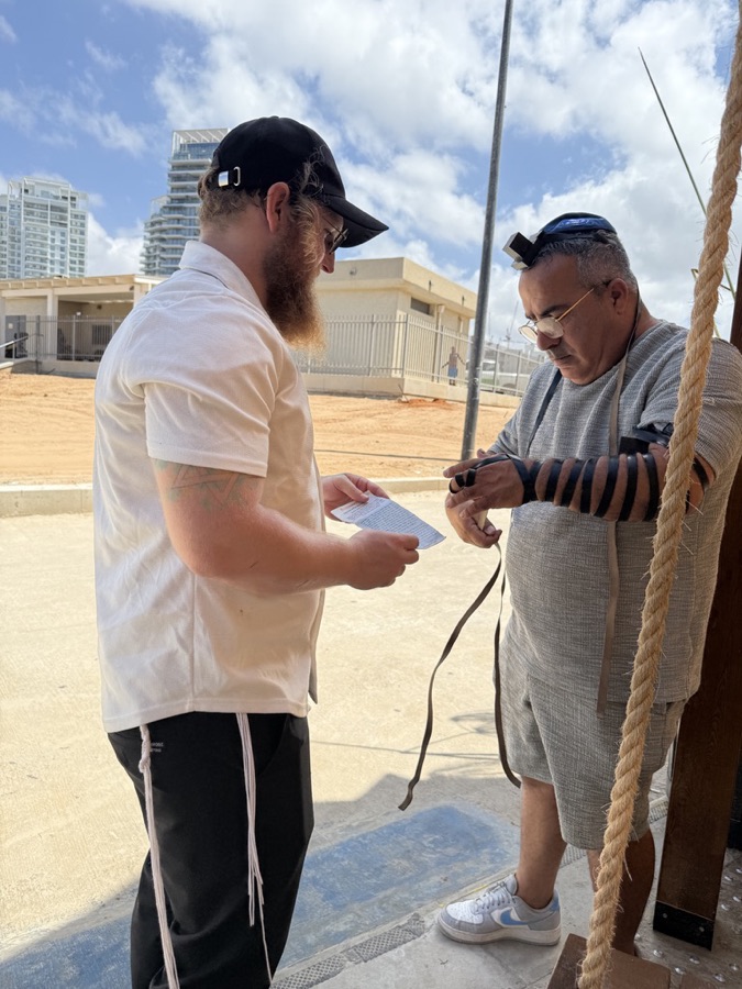 Two people sharing a moment of tefillin and prayer near the Hadera coast