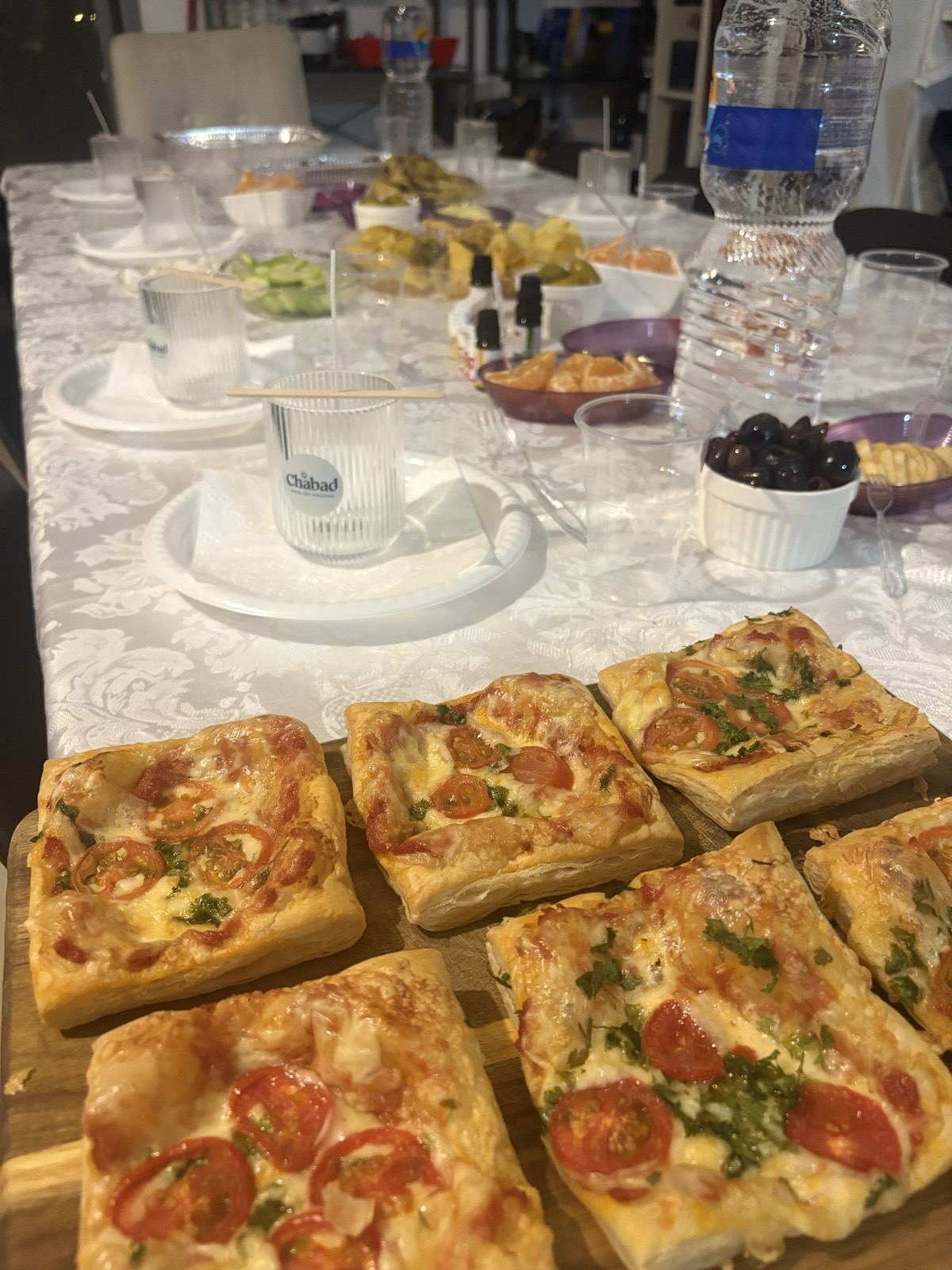 A Shabbat table laid with homemade pizza squares, olives and dishes