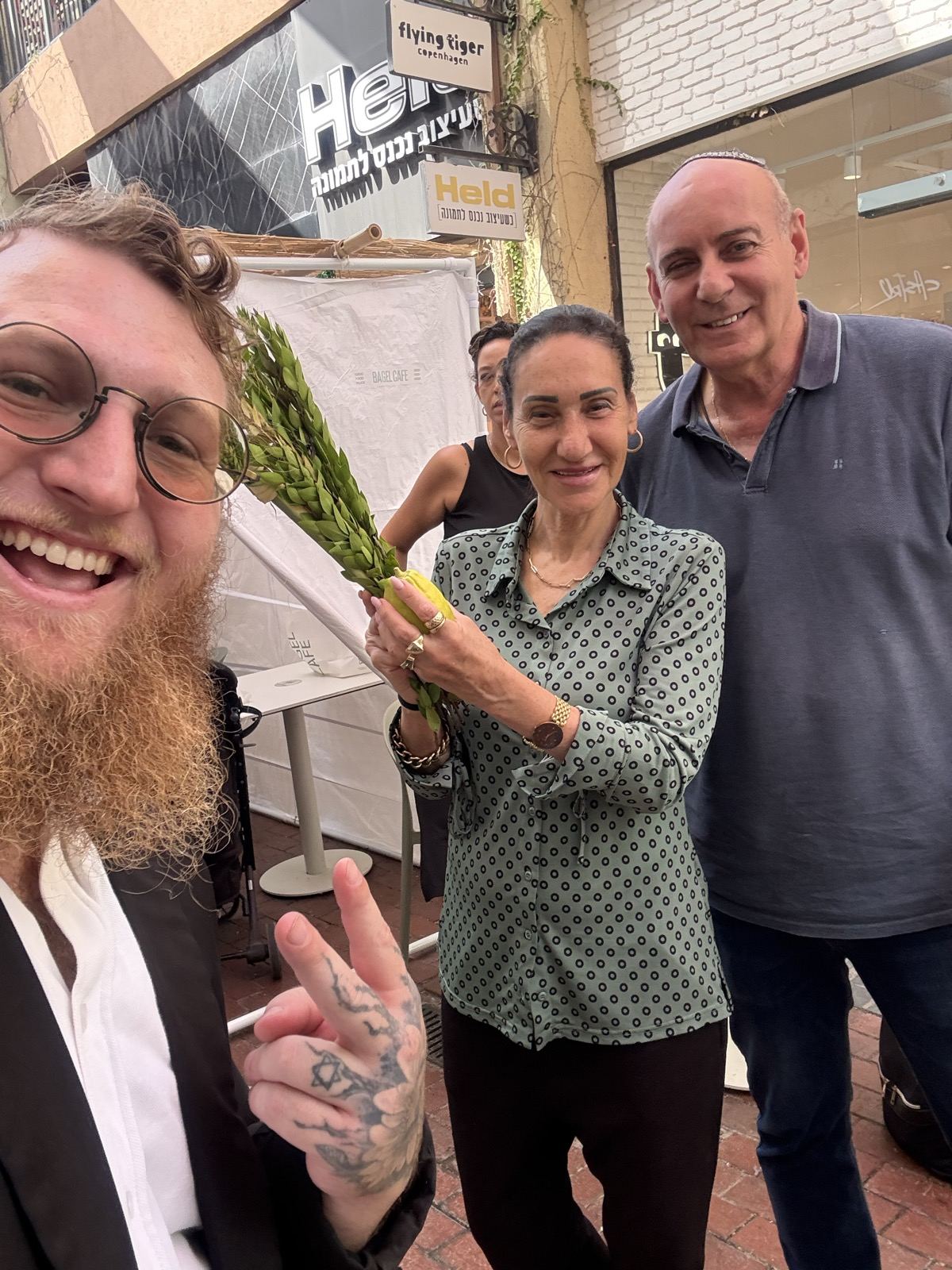 Two smiling people holding a lulav together outside a shop