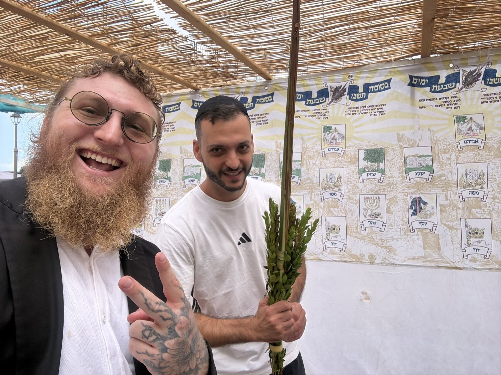 A smiling man holding a lulav under a sukkah roof of bamboo branches