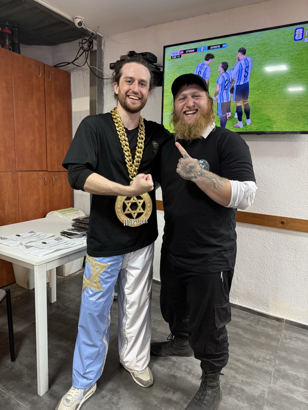 Two men posing together in front of a television showing a football match